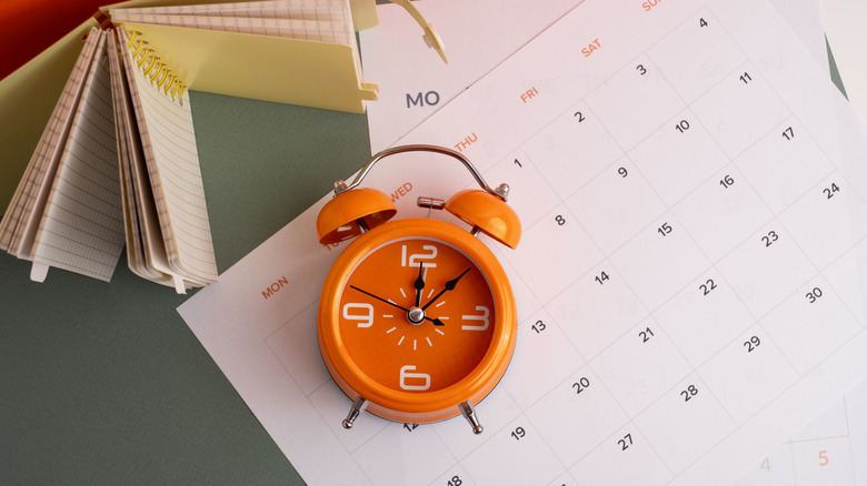 Paper calendar with orange clock placed on top
