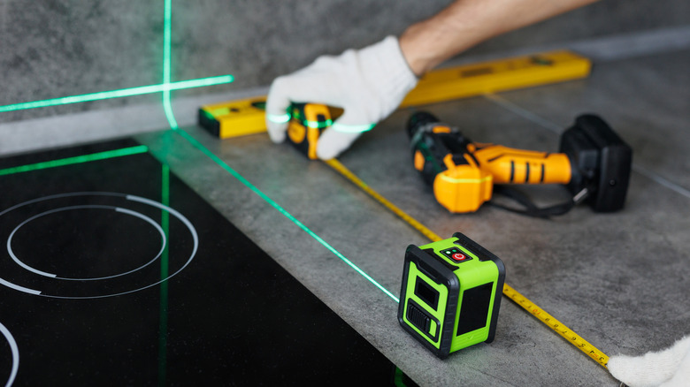 A pair of hands measuring gray kitchen countertop with a tape and laser