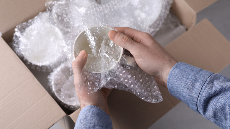 A pair of hands placing ceramic dishware in bubble wrap for storage