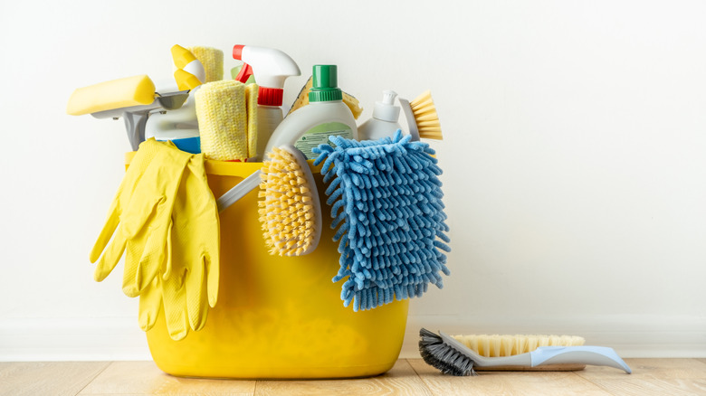 Several cleaning supplies, bottles and cleaning sponges against a white wall