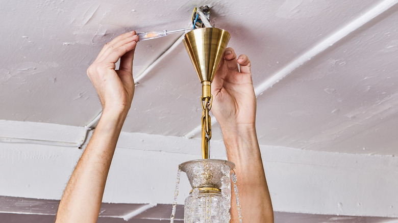 Man disconnecting light fixture from white ceiling