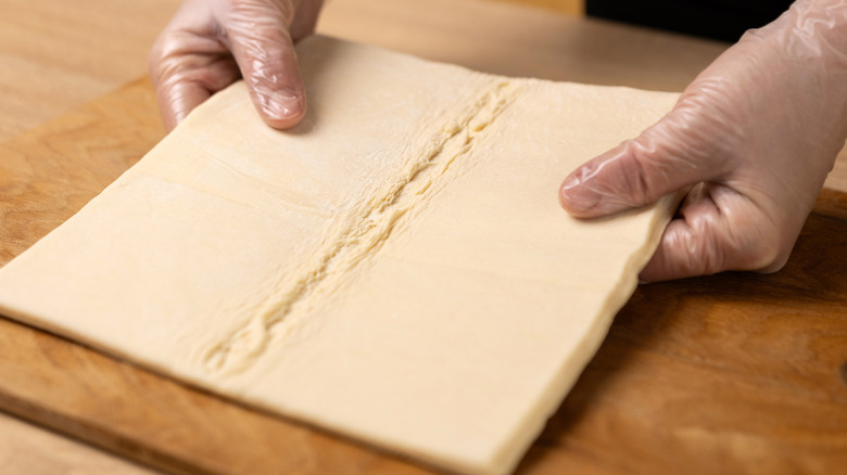 Person wearing gloves, holding a sheet of puff pastry