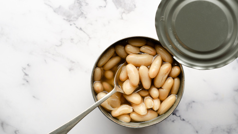 Open can of white beans, with a spoon ready to serve them