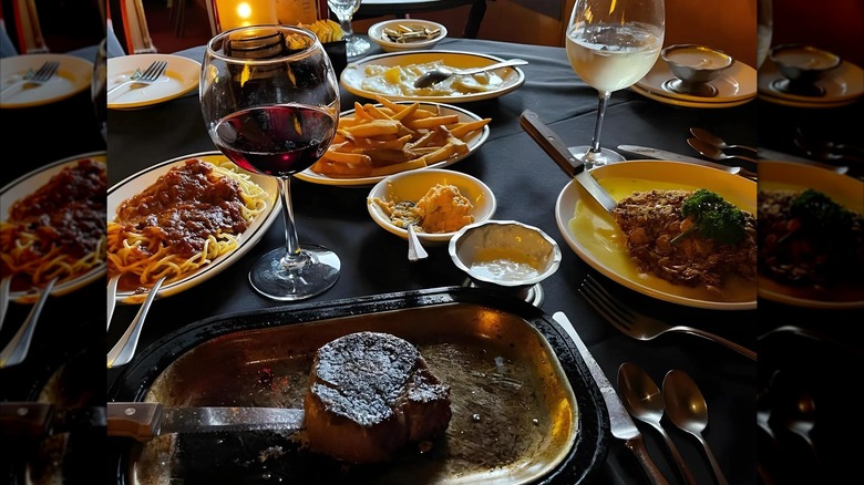 Table set with assortment of pastas, steaks, fries, and wine glasses