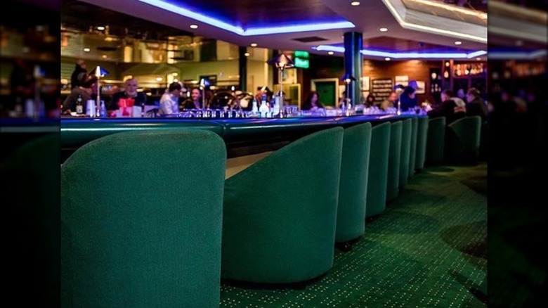 Dark green carpet and chairs at low bar with people in background