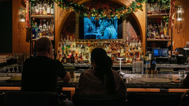 Two people sitting at a bar watching TV