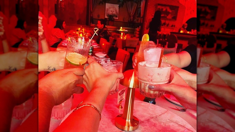 Hands holding cocktails and toasting in red-tinted restaurant