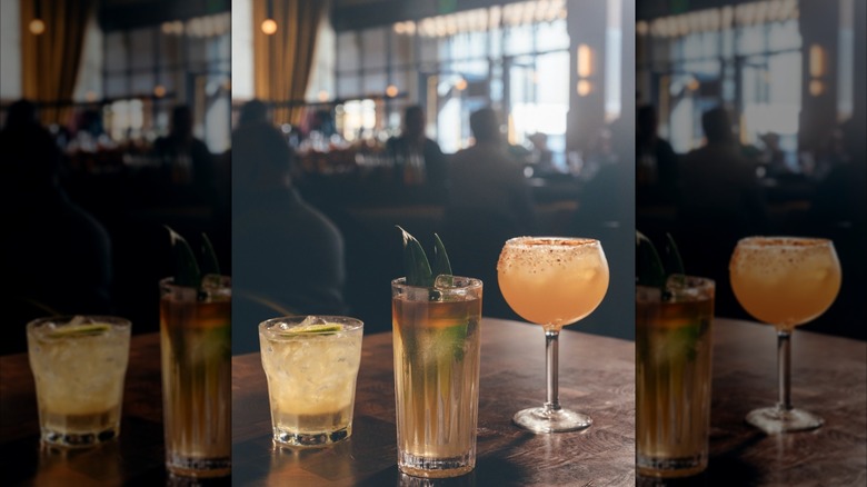 Three cocktails on a wooden table with restaurant blurred in background