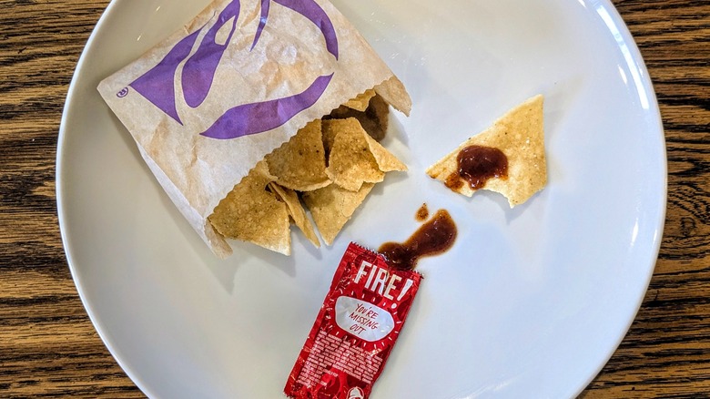 An open packet of Fire sauce and a bag of Taco Bell chips on a white plate