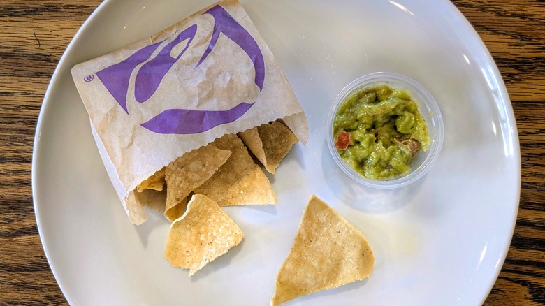 A cup of guacamole and a bag of Taco Bell chips on a white plate