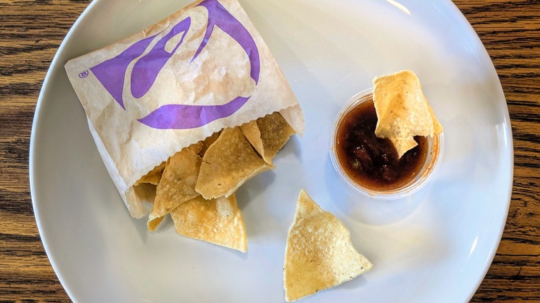 A cup of chunky red sauce and a bag of Taco Bell chips on a white plate