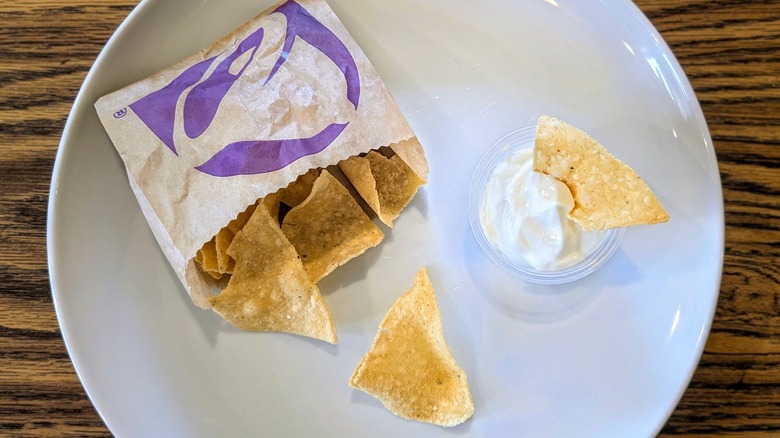 A cup of sour cream and a bag of Taco Bell chips on a white plate