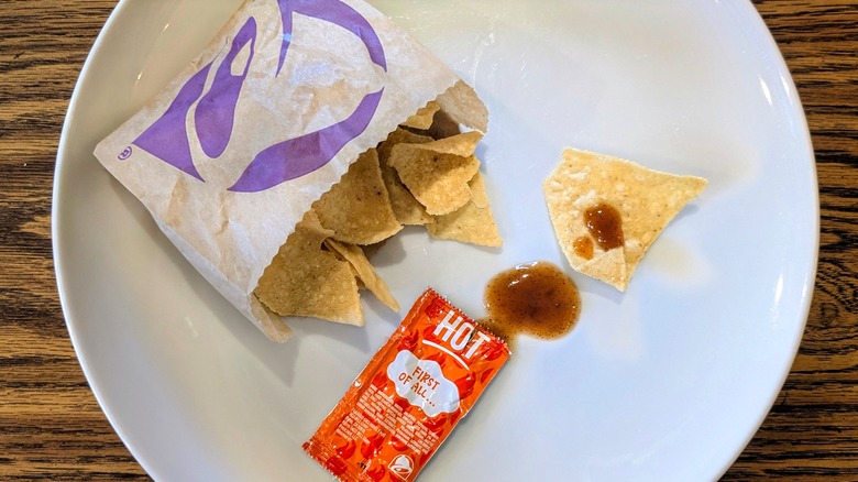 An open hot sauce packet and bag of Taco Bell chips on a white plate