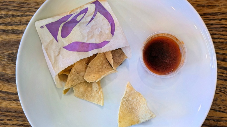 A cup of red sauce and a bag of Taco Bell chips on a white plate