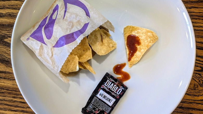 An open packet of Diablo sauce and a bag of Taco Bell chips on a white plate