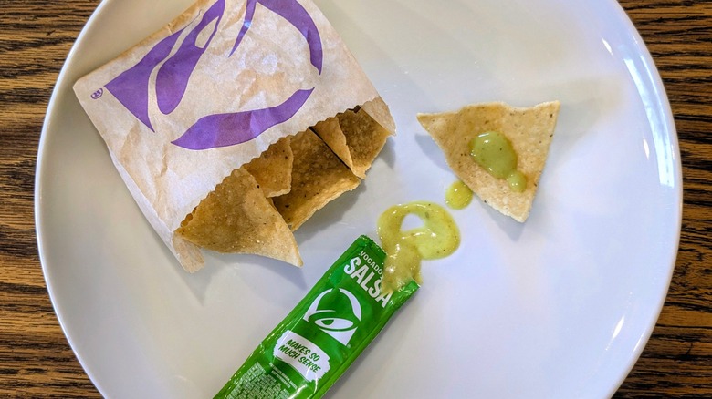 An open packet of salsa verde and a bag of Taco Bell chips on a white plate