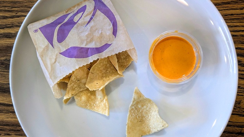 A cup of hot sauce and a bag of Taco Bell chips on a white plate