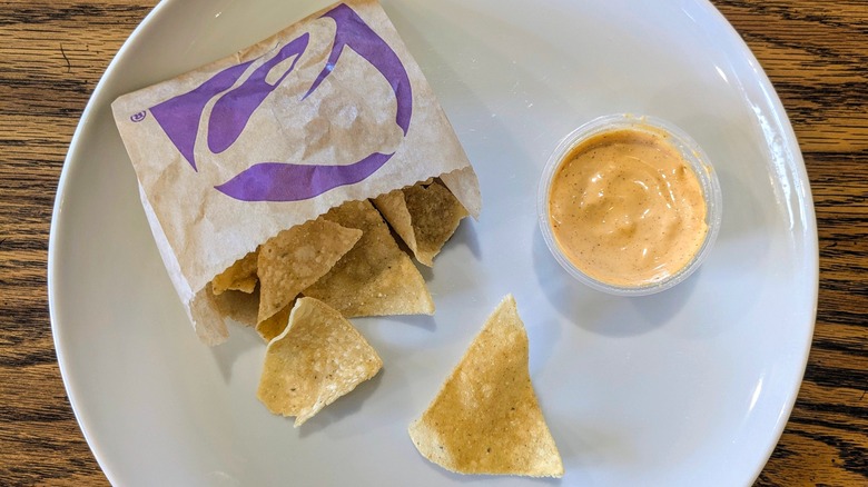 A cup of chipotle sauce and a bag of Taco Bell chips on a white plate