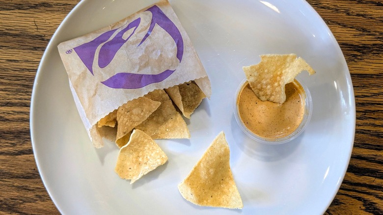 A cup of creamy jalapeno sauce and a bag of Taco Bell chips on a white plate