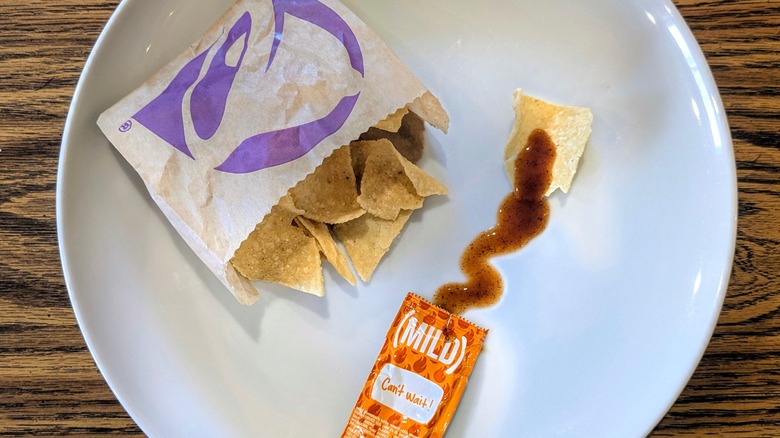 An open hot sauce packet and a bag of Taco Bell chips on a white plate