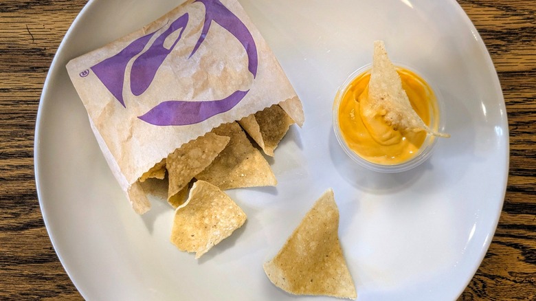A cup of cheese sauce and a bag of Taco Bell chips on a white plate