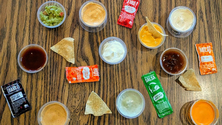 Various sauces in packets and plastic cups scattered on a wood table
