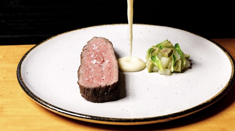 steak and vegetables on a plate with white sauce being pour in the middle