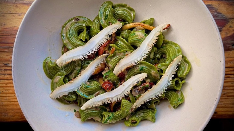 white dish with curly green pasta and wild mushrooms