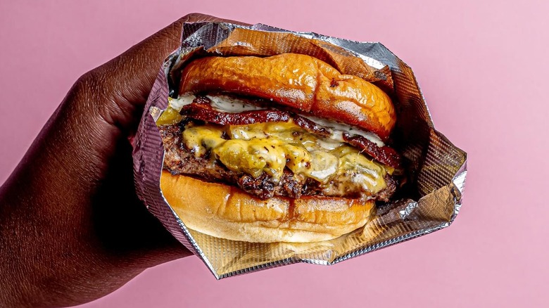 man's hand holding burger wrapped in foil