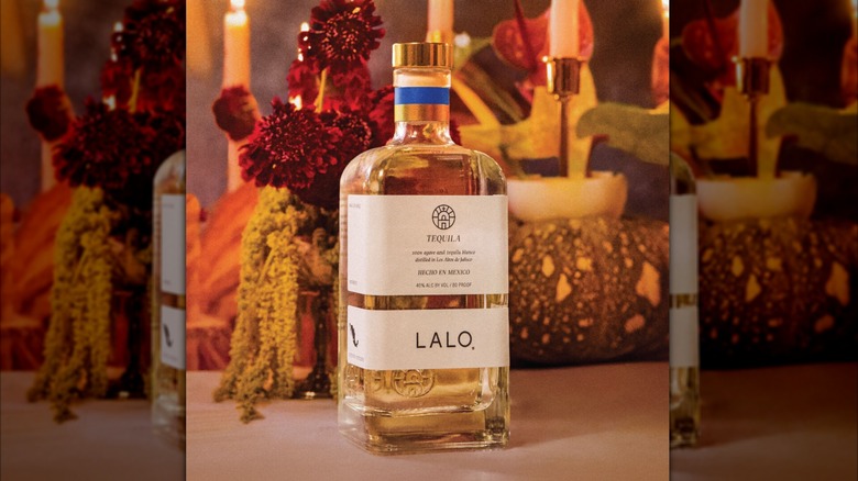 A bottle of Lalo on a table surrounded by candles and flowers