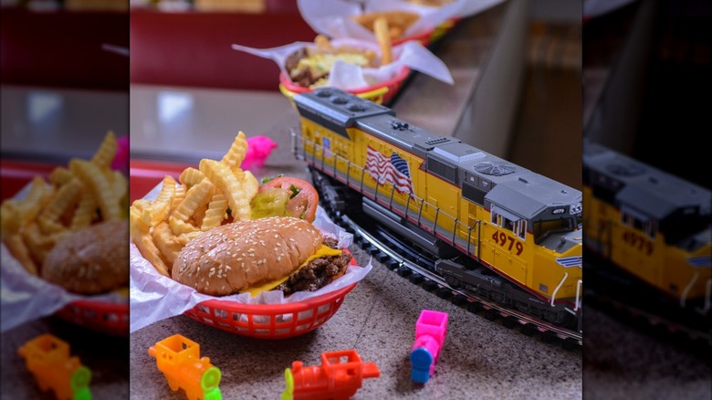 A cheeseburger and fries in a basket on a diner counter with toy trains