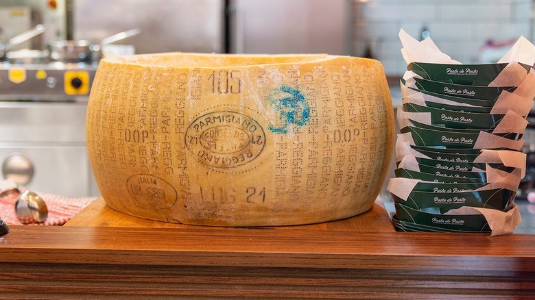 a parmesean cheese wheel on a wooden counter next to take-out containters