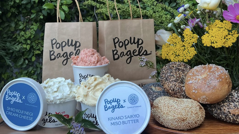 open cream cheese containers alongside bagels and brown paper bags.