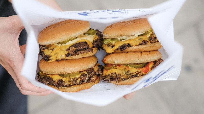 hands holding out burgers in a to-go container