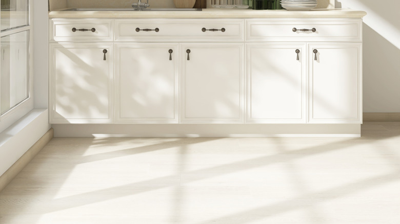 White wood laminate flooring in natural sunlight against white cabinets