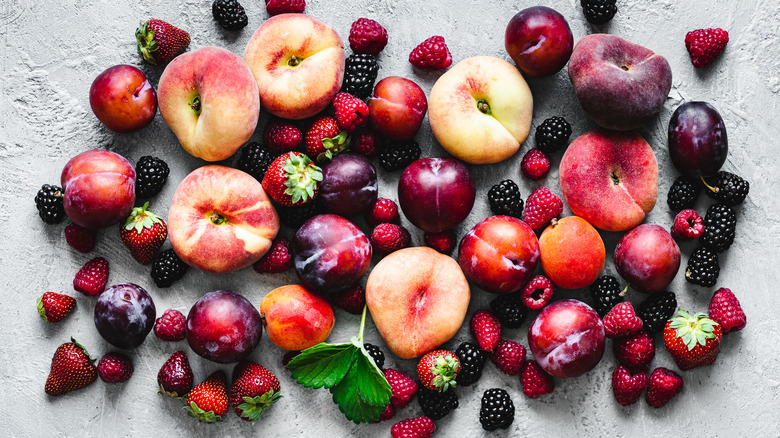 An assortment of peaches, plums, and berries on a rustic grey background