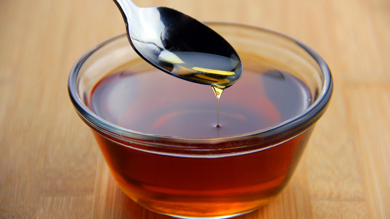 A close up of maple syrup dripping from a spoon into a glass bowl