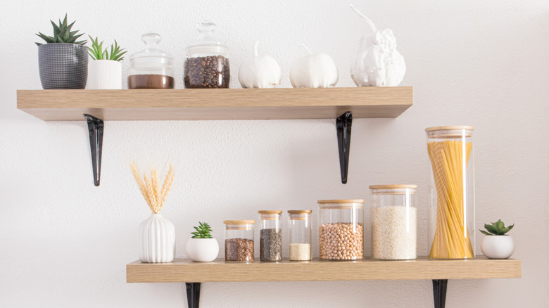 Open wooden shelves in a kitchen with storage jars against textured a white wall