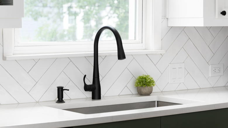 Sink detail in a moden kitchen with white herringbone tiles on the backsplash