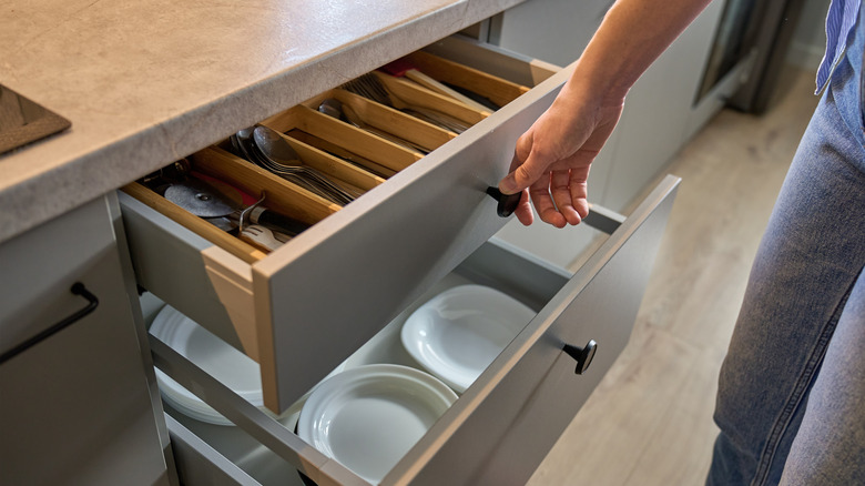 Person open kitchen drawer with various utensils sorted in a tray