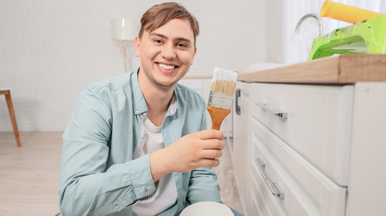 Young man holding a brush while painting a kitchen drawer