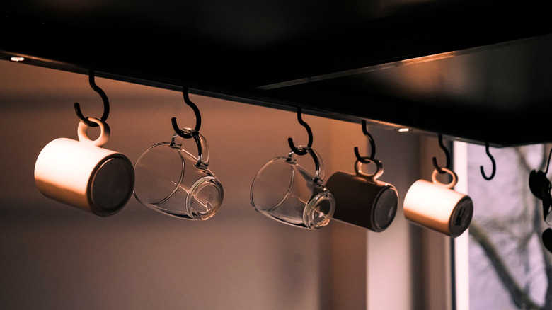 Mugs hung on hooks under kitchen shelf