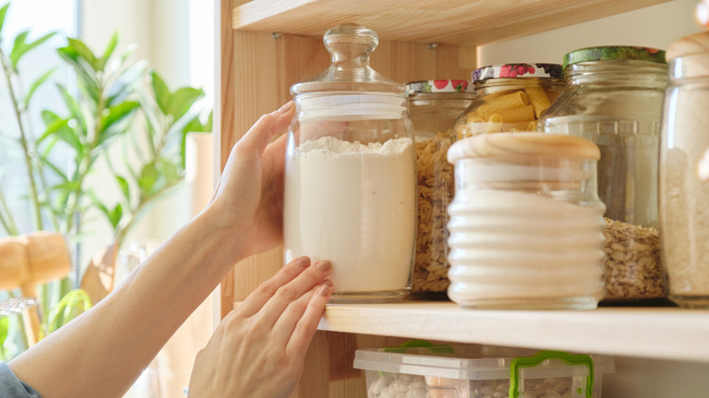 Female hands taking out jar of flour from crowded kitchen cabinet