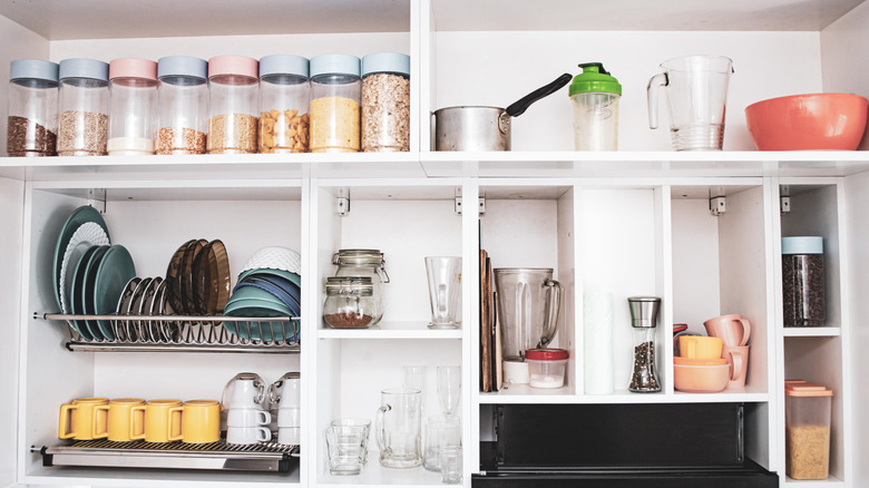 Neatly organized kitchen cabinet with colour coordinated jars, dishware, mugs and other essentials