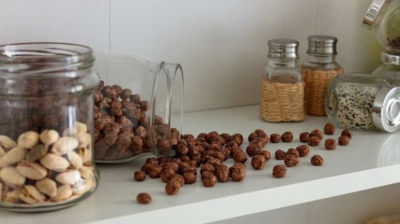Cluttered kitchen cabinet shelf with spilled cereal and oddly stacked jars