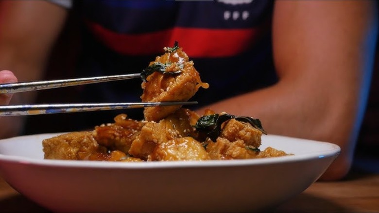 A person holds san bei tofu with chopsticks over a bowl