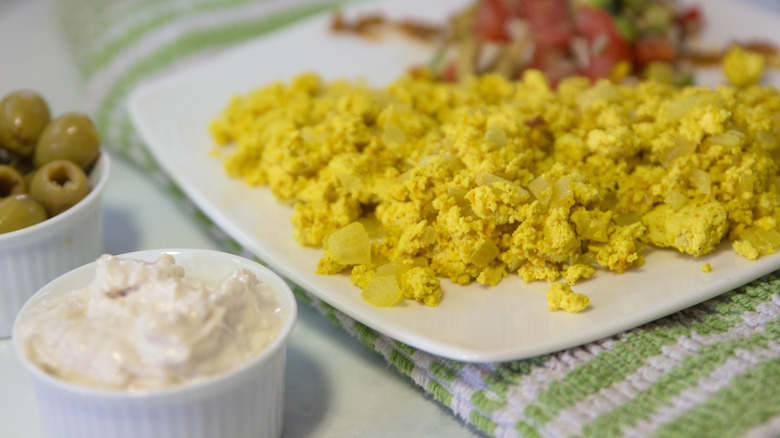 A plate of scramble tofu next to dip and olives