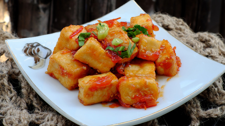 Fried tofu with tomato sauce on a plate with spring onions