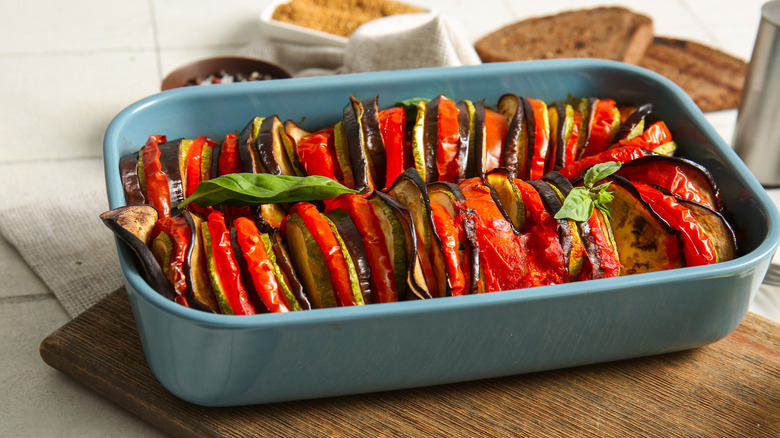 Bbaking dish with ratatouille on a wooden board placed on the counter