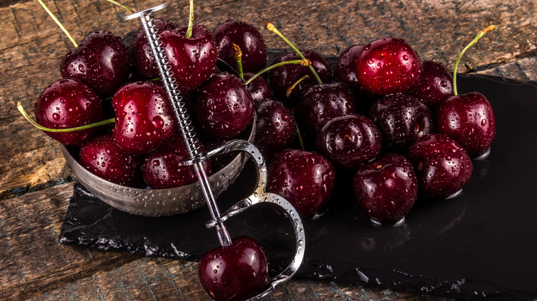 cherry pitting tool surrounded by fresh cherries